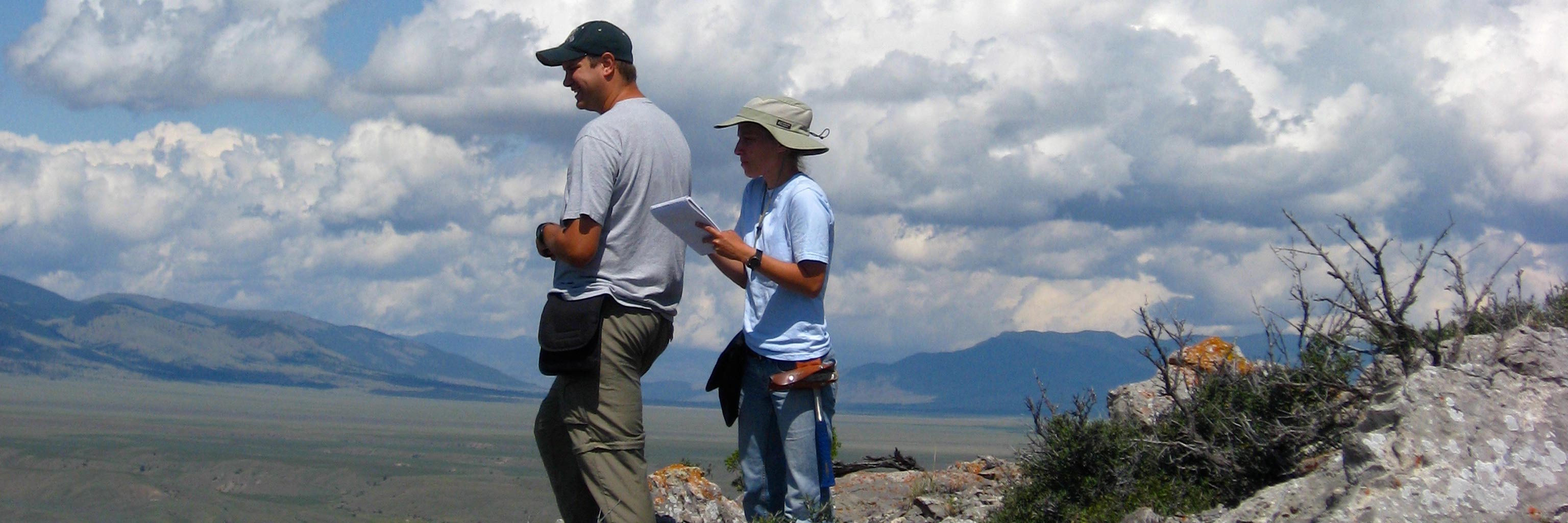 two students standing over a ridge documenting the land