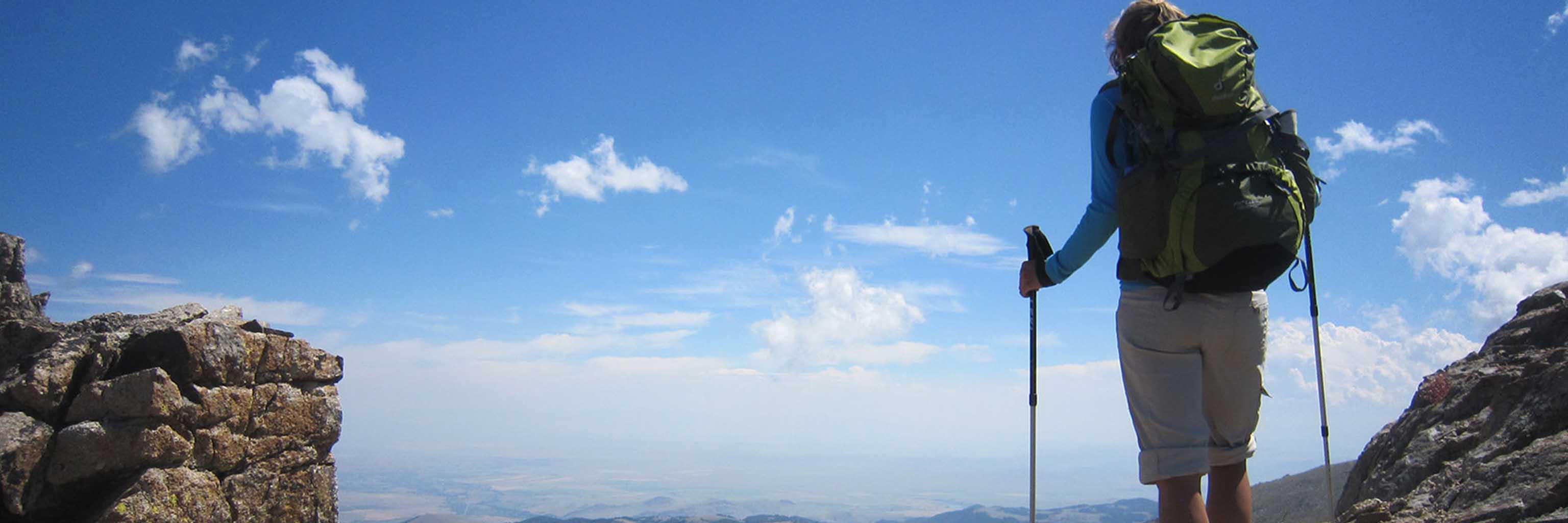 hiker with hiking sticks look out onto the landscape from a mountain top
